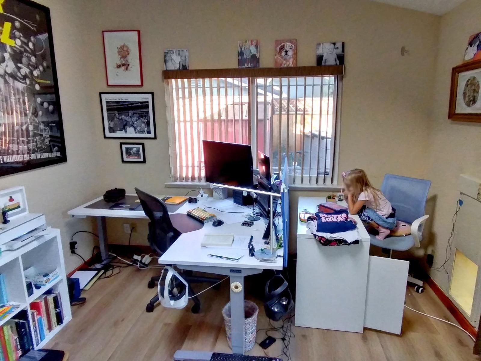 A home office with a standing desk, and a child sitting on an office chair beside it.